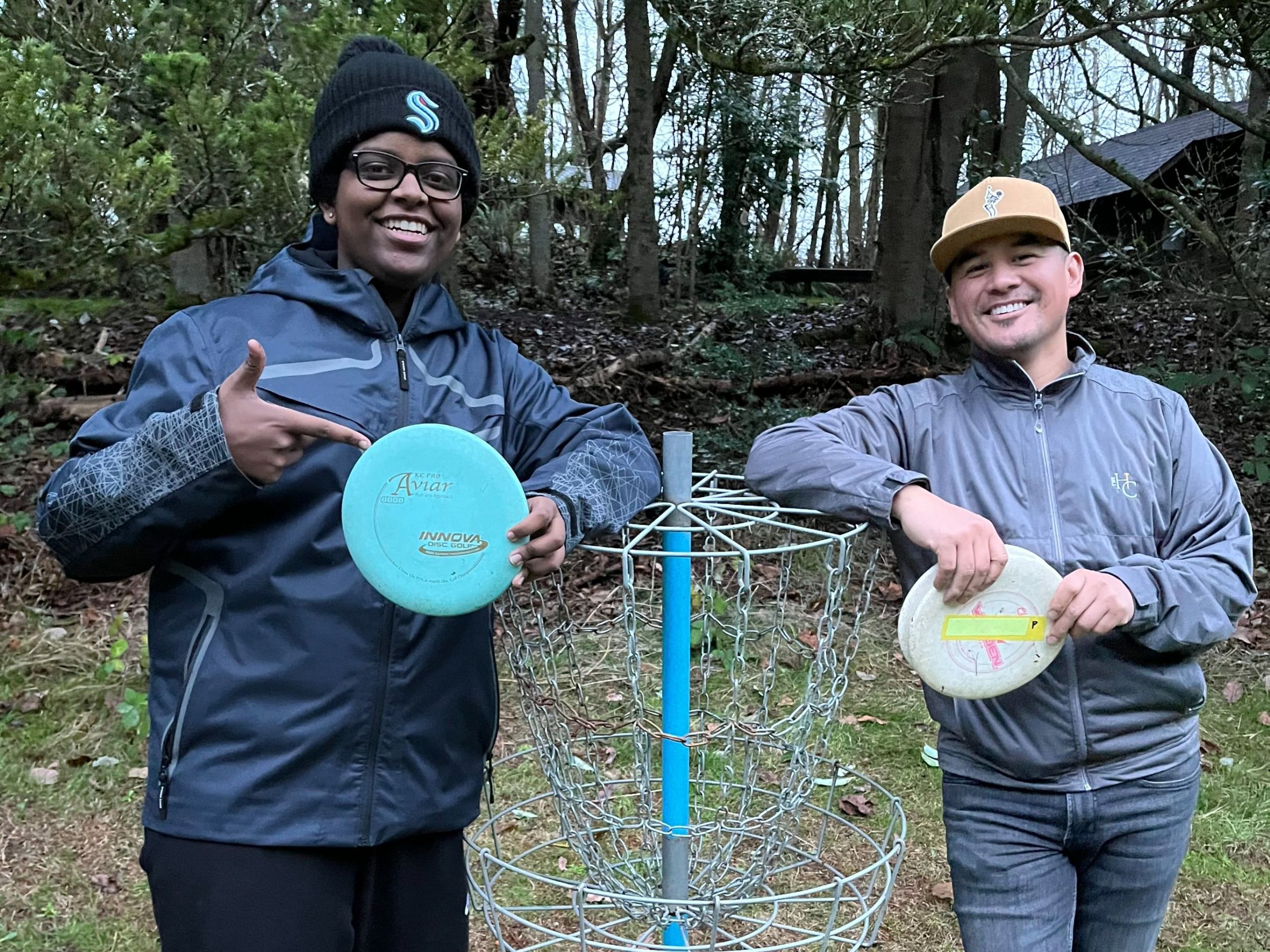 Two smiling people holding discs near a disc golf basic