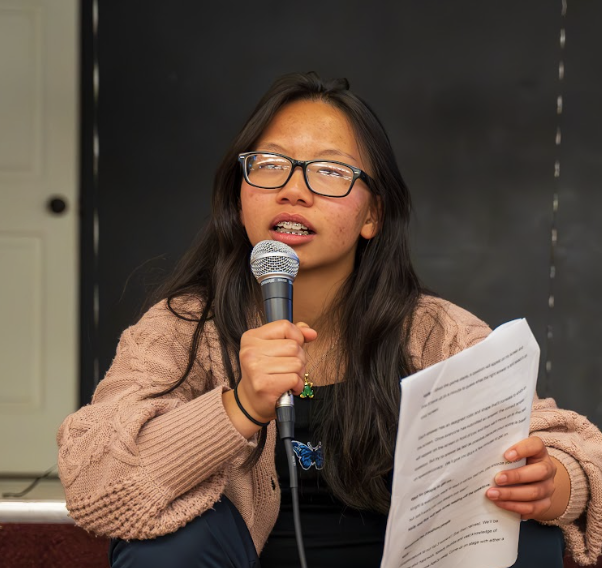 young asian woman in glasses speaks into microphone while holding a script
